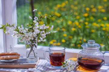 Hot tea in glass teapot and cup on windowsill at home