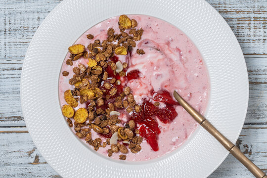 White plate with red strawberries, granola and natural yogurt on a black background, top view