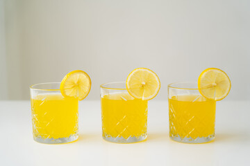slices of fresh lemon on glasses with natural citrus juice on white surface isolated on grey.