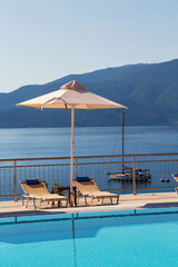 Luxury swimming pool with empty deck chairs and umbrella at resort with beautiful sea view