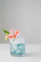 pink alstroemeria flower in glass with iced tonic on white surface isolated on grey.