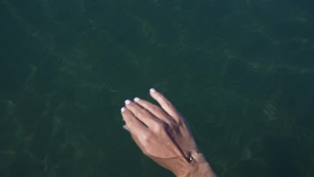 Closeup first person top view 4k stock video footage of one female hand touching and holding transparent sea water on sunny tropical beach during summer vacations. Female hand isolated on water