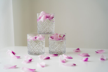 crystal glasses with tonic and floral petals on white surface and grey background.