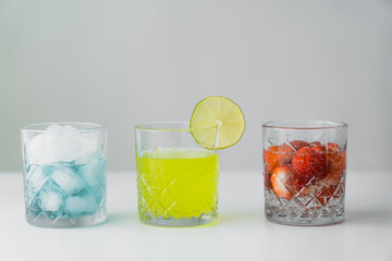 lemonade and strawberry tonic near glass with ice cubes on white surface isolated on grey.