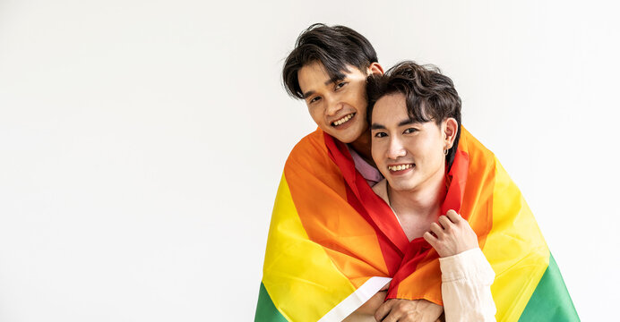 Guys spend time together at home, Portrait of Happy Asian gay couple embracing and showing their love under lgbt colorful rainbow flag. LGBT and love concept.