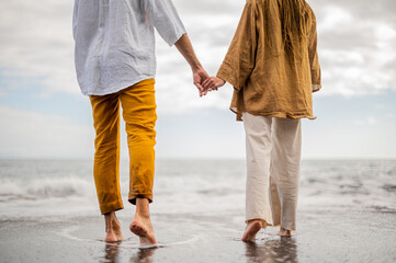 Young loving couple shown from behind holding hands on a beach - obrazy, fototapety, plakaty