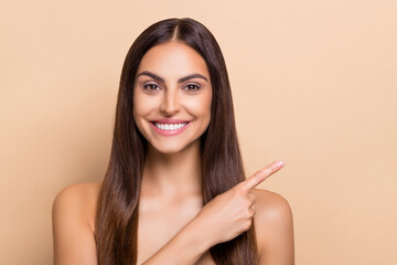 Portrait of attractive cheerful long-haired girl demonstrating copy space ad sale isolated over beige pastel color background