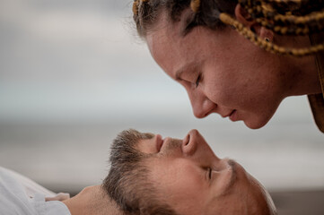 Fototapeta premium Young couple lying on the beach holding heads close to each other 