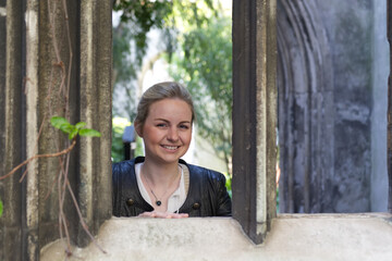 Beautiful young blonde woman with necklace looks through a window arch of an old church ruin (St. Dunstan in the East)