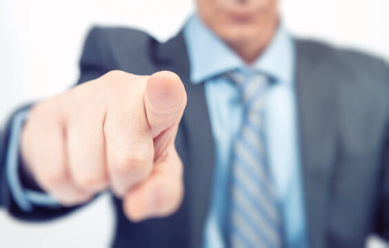 Businessman in a dark jacket points at you with his finger, shallow depth of field.