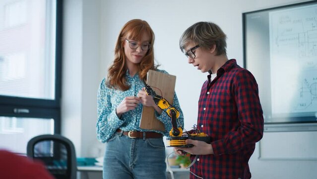 College student presenting his builded robotic toy to young science teacher at robotics classroom at school.