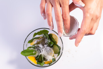 preparation of a refreshing cosmetic mask girl's hands sprinkling clay ingredients salad on white background