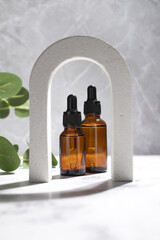 Cosmetic bottles serum or oil in arch on grey marble background. Natural cosmetics concept, skin care product. Beauty concept for face body care