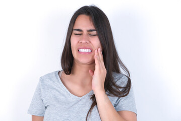 Young beautiful brunette woman wearing grey T-shirt over white wall touching mouth with hand with painful expression because of toothache or dental illness on teeth.