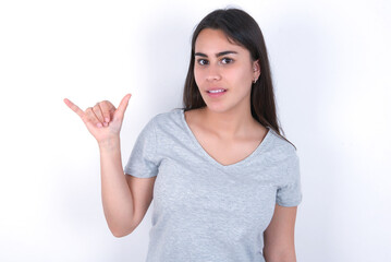 Young beautiful brunette woman wearing gray T-shirt over white wall showing up number six Liu with fingers gesture in sign Chinese language