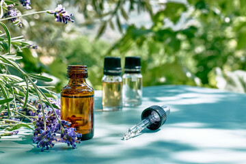 Dropper bottle with natural essential lavender oil and purple lavender flowers on turquoise surface against nature green background. Aromatherapy, alternative medicine and perfumery concept.Copy space