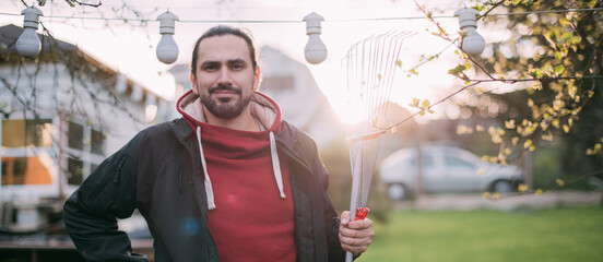 Portrait of a gardener - a young man with a garden tool in his hands in the garden in the evening at sunset.