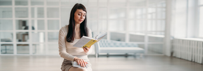 Portrait of a young beautiful woman with books in her hands in a large bright room. Beautiful brunette, young teacher or student
