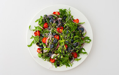 Light salad with arugula and berries, strawberries and blueberries, delicious healthy summer salad on a white background