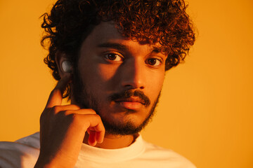 Young curly man in earphones posing and looking at camera