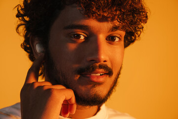 Young curly man in earphones smiling and looking at camera