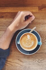 Artfully crafted cafe latte with a male hand next to the cup.
