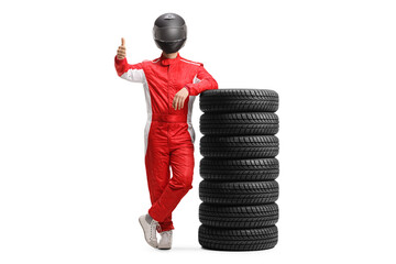 Full length portrait of a motorsport racer in a red suit leaning on a pile of tires and showing...