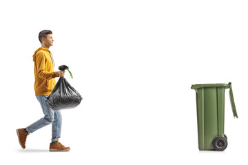 Full length profile shot of a guy carrying a plastic waste bag and walking towards a dustbin