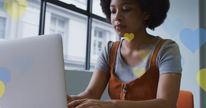 Animation of hearts falling over african american woman using laptop