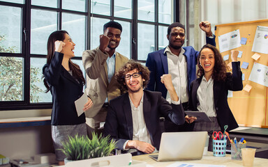 Group of diverse multiethnic businesspeople wearing formal suits, raising hands, smiling together with happiness and success, standing in modern indoor office after finishing teamwork project.