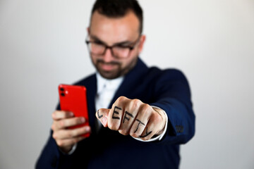 handsome dark-haired man, in a navy blue suit, raises his left hand with his left fist clenched for the day of the left-handed and clutching his red cell phone in his right hand.
