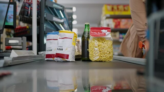 Cropped view of young woman shopping in supermarket, putting products on checking desk