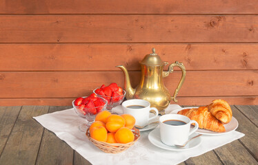 Coffee pot, two cups of coffee, fruits and croissants on aged wooden table. Selective focus.