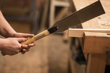 Cropped close-up hands of joiner, carpenter holding and using chisel or rasp with plank lumber on...