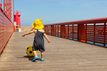 boy in yellow hat playing ball on red bridge