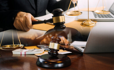 Justice and law concept.Male judge in a courtroom with the gavel, working with, computer and docking keyboard, eyeglasses, on table in morning light