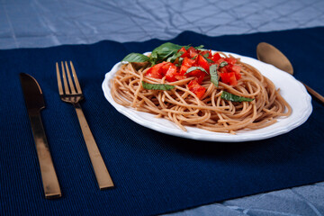 Vegetarian pasta with tomatoes and basil, served plate and fork on the table with a blue tablecloth, restaurant pasta serving