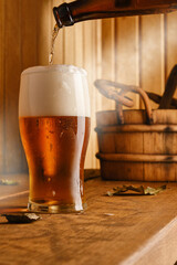 Light beer pouring from a bottle into a mug in the interior of the bath. Glass of lager beer, wooden bucket and ladle in the interior of the sauna. Shallow depth of field. 