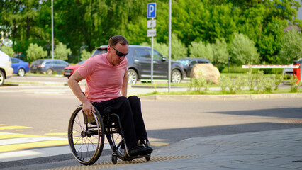 Caucasian man in a wheelchair drives onto the sidewalk
