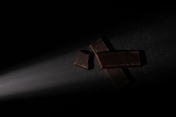 Pieces of chocolate bar illuminated with a soft point light, with an overhead view, on a black background