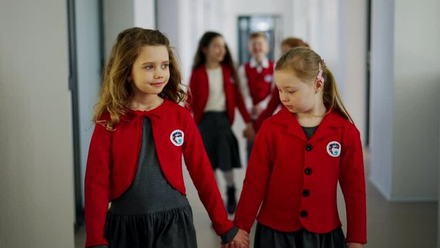 Happy schoolgirl with Down syndrome in uniform walking in scool corridor with classmates.