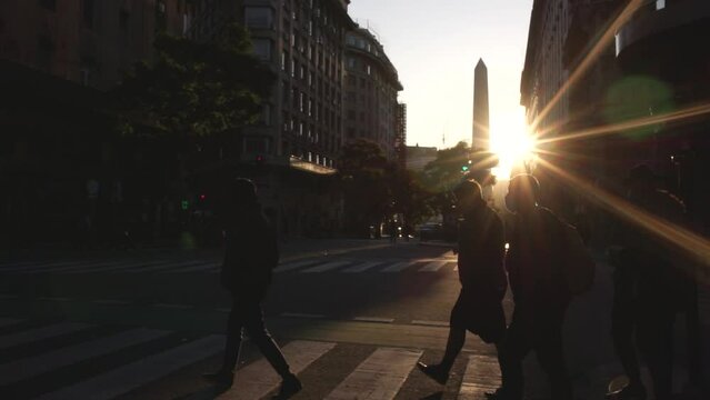 People crossing Corrientes Avenue with sunset and the obelisk at background, Buenos Aires, Argentina