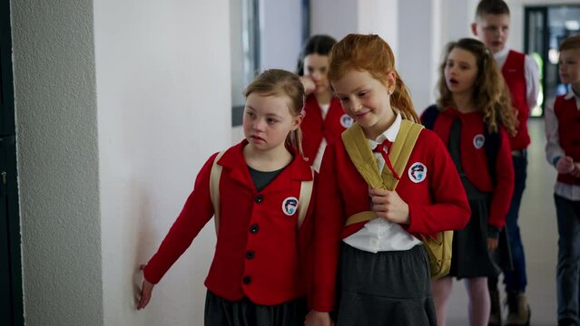 Happy schoolgirl with Down syndrome in uniform walking in scool corridor with classmates.
