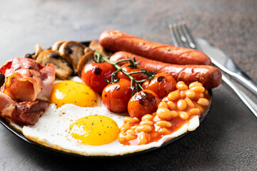 English breakfast with fried eggs, sausages, bacon, beans, mushrooms, toasts on white plate at the...