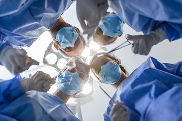 Surgeons standing above of the patient before surgery. Multi-ethnic healthcare workers performing surgery on patient at operation theater. - obrazy, fototapety, plakaty
