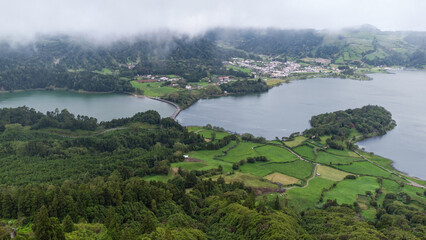 The green and blue volcanic crater lakes of Sete Cidades, located on the Azores, Portugal island of Sao Miguel, are shown from an elevated view on a cloudy day.