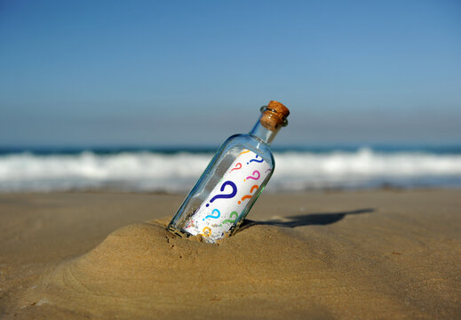 Botella encontrada en la playa con preguntas de colores en su interior. Muchas inc&oacute;gnitas. Concepto de incertidumbre sobre el futuro