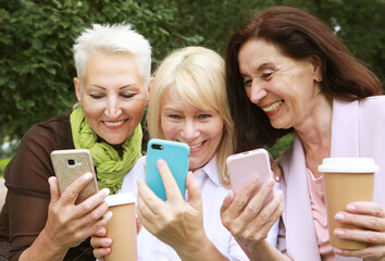 Charming old women laugh merrily and look at the screens of their smartphones. - obrazy, fototapety, plakaty