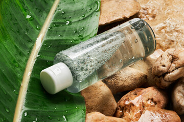 Transparent bottle of micellar water with fresh leaf on natural stone background. Liquid tonic or...