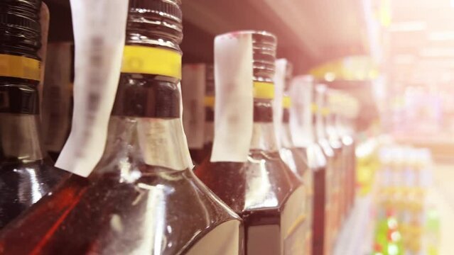 Bottles of whiskey, brandy or Scotch line up on the shelves of a liquor store or ABC store. Close-up shot